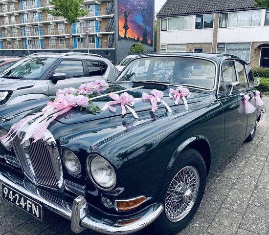Donkergroene trouwauto met roze bloemen en linten op de motorkap, met kenteken 94-24-FN.