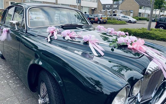 Donkergroene trouwauto met roze bloemen en linten op de motorkap.