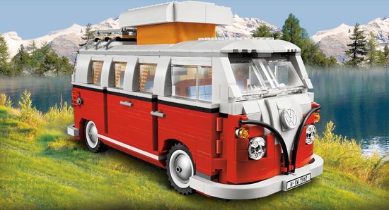 Rode LEGO camperbus met witte opbouw, geparkeerd aan de rand van een meer met bergen op de achtergrond.