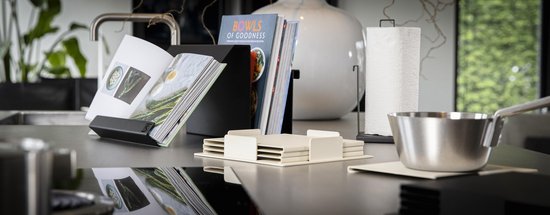 Lichtbeige onderzetters op een aanrecht met een kookboek, keukenrol en pan.
