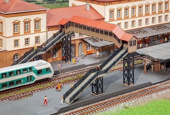Gedetailleerd diorama van een overkapte voetgangersbrug bij een station met een trein en miniatuurpassagiers.