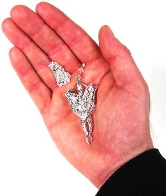 Zilverkleurige Arwen Evenstar hanger met sprankelende kristallen, gehouden in een hand. Naast de hanger ligt een losse druppelvormige kristal.