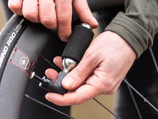 Handen gebruiken een zilveren CO2-patroon met zwarte hoes om een fietsband op te pompen.