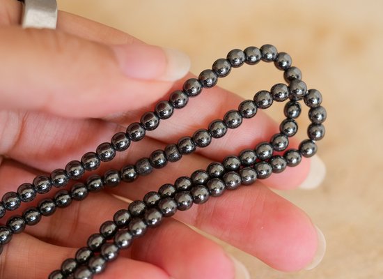 Hand van een persoon die een dunne, donkergrijze hematite kralen armband vasthoudt.