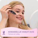 Een lachende blonde vrouw met een lichte huid gebruikt de zwarte laser plasmabehandelingspen op haar gezicht.