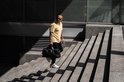 Man met geel poloshirt, zwarte jeans en een zwarte sporttas die een trap oploopt.