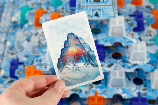 Hand die een kaart vasthoudt met daarop een besneeuwde blauw-oranje piramide, met op de achtergrond een spel met ijsblokken.
