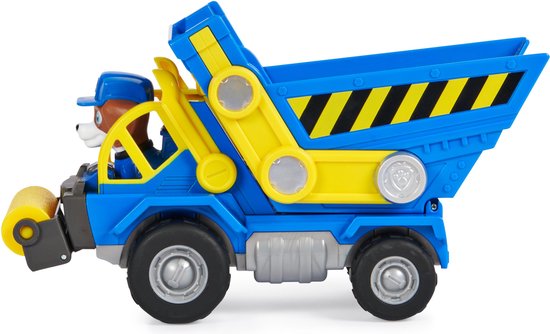 Zijaanzicht van blauwe kiepwagen met gele onderdelen, hondje in de cabine, met gele roller aan de voorkant.