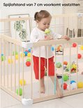 Houten babybox met een kind dat een fles drinkt, met een meting van de spijlafstand.