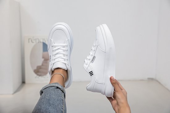 Witte lage sneakers met veters, gedragen door een persoon met spijkerbroek en enkelbandje.