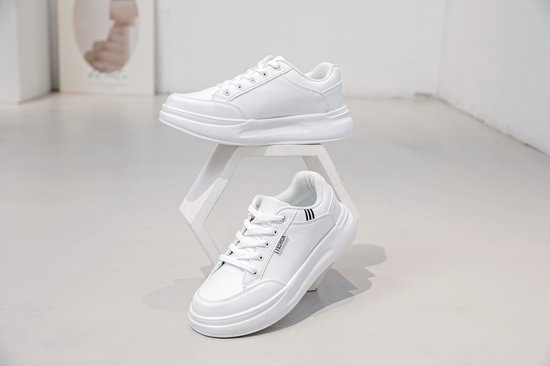 Twee witte lage sneakers met veters, één op een decoratieve standaard.