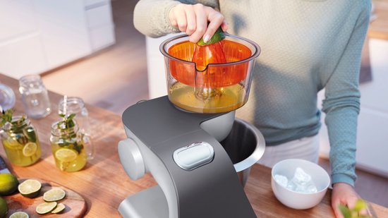 Robot de cuisine gris avec presse-agrumes, une femme presse une orange.