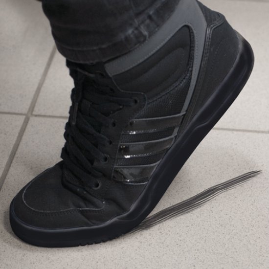 Zwarte adidas high-top sneaker met veters aan een voet in een grijze broekspijp, staand op een tegelvloer.