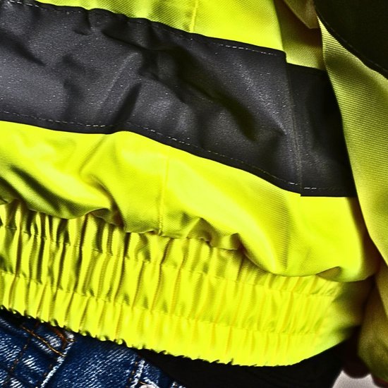 Onderkant van een felgele jas met grijze reflecterende strepen en een elastische tailleband met kreukels.