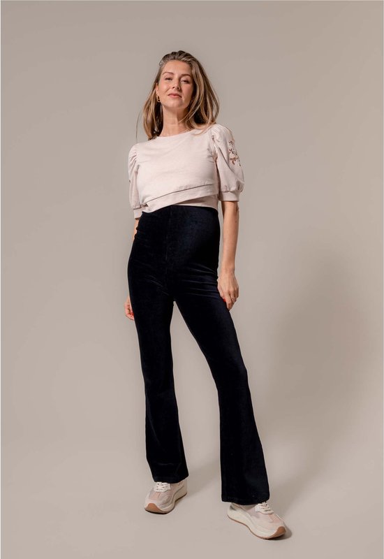 Model draagt een lichtroze top met pofmouwen en zwarte flared broek.