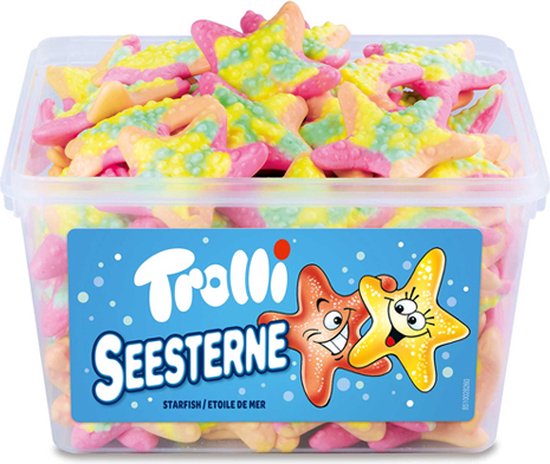 Een transparante bak gevuld met kleurrijke zeestervormige snoepjes in roze, geel en groen. De deksel toont het Trolli logo en twee lachende zeesterren, met de tekst 'SEESTERNE STARFISH ÉTOILE DE MER'.