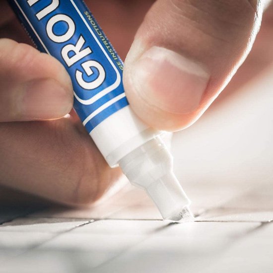Dichtbij hand die witte voegpen gebruikt om voegen tussen witte tegels te verven.