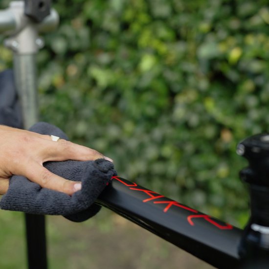 Hand veegt met donkere doek over een zwarte fiets met rode opdruk 'DART'.