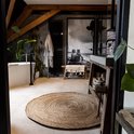 Een rond, natuurlijk jute vloerkleed in een badkamer met een kunstwerk van een strandscène.