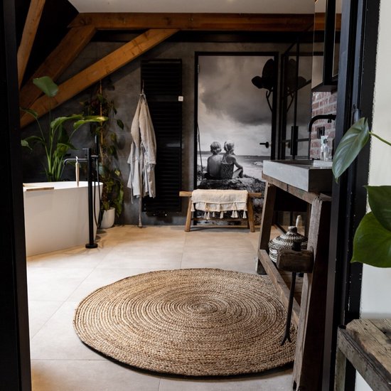 Een rond, natuurlijk jute vloerkleed in een badkamer met een kunstwerk van een strandscène.