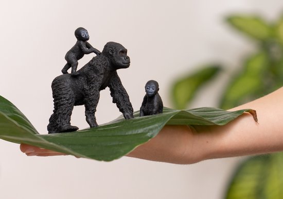 Een Schleich gorilla familie set op een groot groen blad, met een jong op de rug van de moeder.