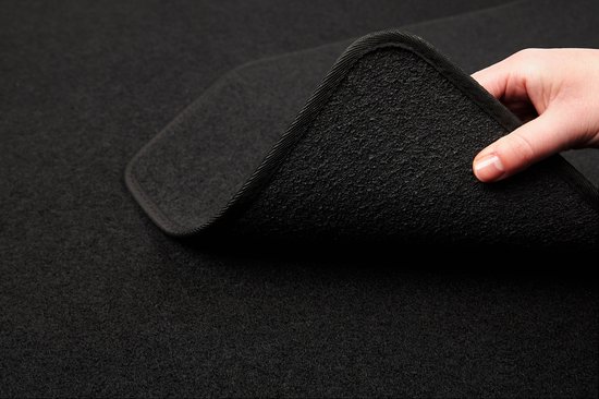 Main montrant l'épaisseur et la texture d'un tapis de voiture noir avec un bord fini.