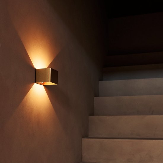 Gouden vierkante wandlamp die licht geeft op een donkere trap.