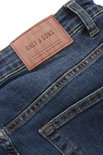 Bruin leren merklabel op een donkerblauwe spijkerbroek met gele stiksels.