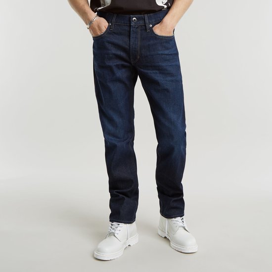 Model draagt een donkerblauwe G-Star Mosa Straight jeans met witte veterschoenen.