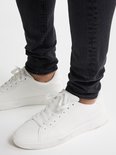 Onderlichaam van een man in een strakke zwarte spijkerbroek en witte sneakers met veters.