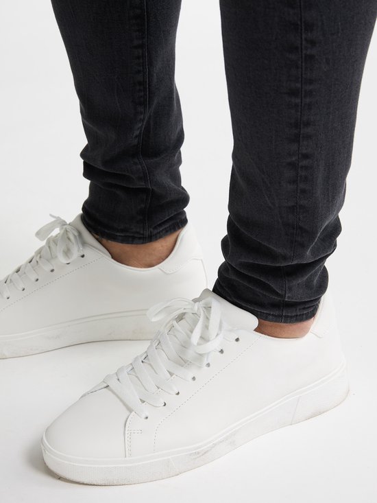 Onderlichaam van een man in een strakke zwarte spijkerbroek en witte sneakers met veters.