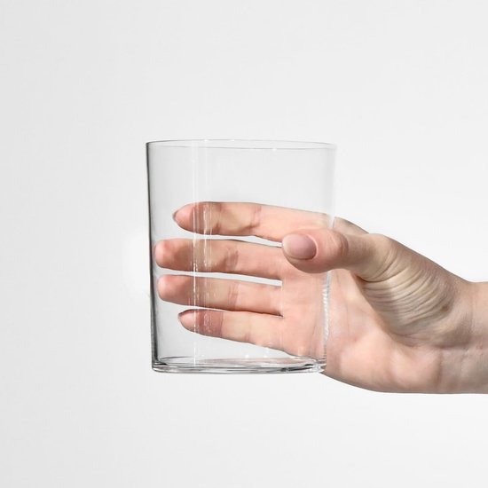 Een hand die een leeg, cilindrisch, glazen waterglas vasthoudt.
