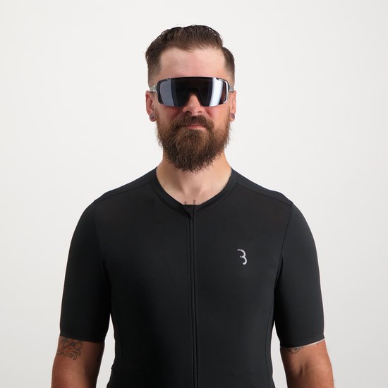 Man met baard draagt een zwarte fietsoutfit en een oversized fietsbril met donkere, spiegelende lenzen.