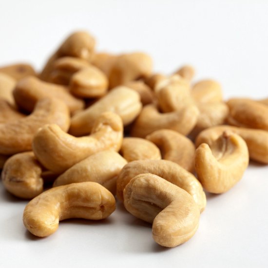Een hoopje geroosterde cashewnoten met een goudbruine kleur op een witte achtergrond.