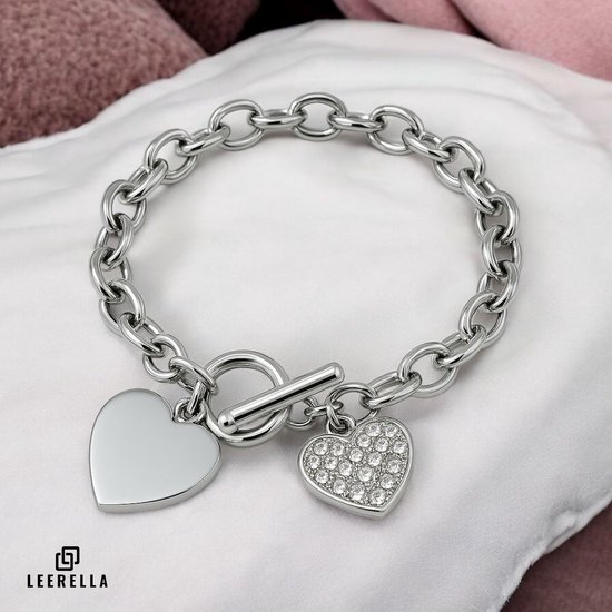 Zilverkleurige schakelarmband met een gladde hartvormige hanger en een hartvormige hanger met zirkonia's, op een witte satijnen stof.