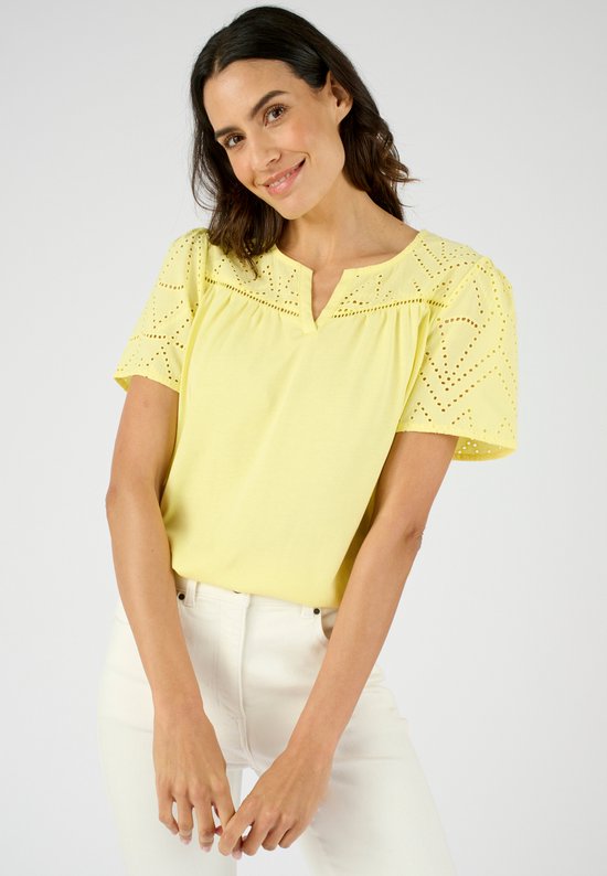 Mannequin portant un t-shirt jaune pâle en coton à manches courtes, col en V et broderie anglaise sur les épaules et les manches. Elle porte un pantalon blanc.