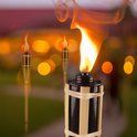 Close-up van een brandende bamboe tuinfakkel met wazige lichtjes op de achtergrond.