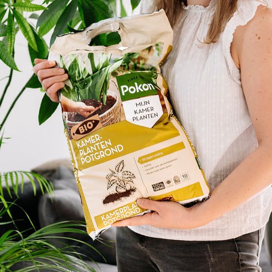 Vrouw houdt zak Pokon BIO Kamerplanten Potgrond vast bij een kamerplant.
