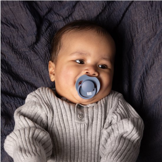 Baby met een lichtblauwe Difrax Prime fopspeen in de mond, liggend op een donkerblauwe stof.
