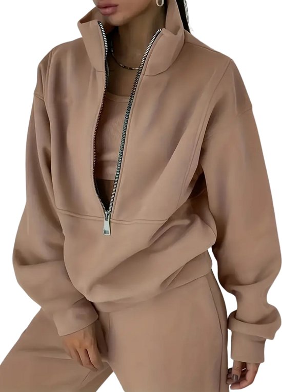 Mannequin portant un survêtement beige zippé. Le sweat à capuche à col montant a une fermeture éclair argentée et est combiné avec un crop top et un pantalon de jogging.