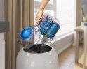 Une femme vide le bac à poussière de l'aspirateur Philips rouge et noir dans une poubelle blanche.