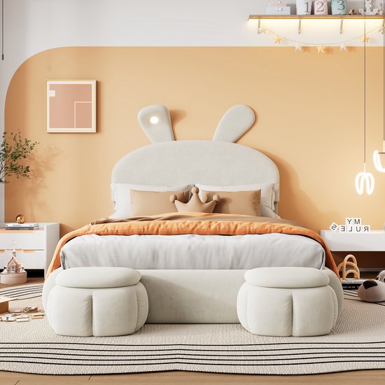 Wit kinderbed met konijnenoren hoofdbord, oranje dekbed en twee ronde krukken.