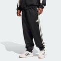 Man in zwarte trainingsbroek met witte strepen en Adidas logo, gedragen met witte sneakers.