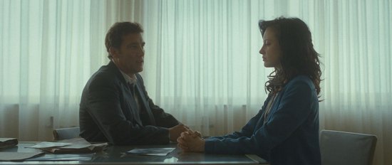 Man en vrouw zitten aan tafel, handen vasthoudend voor een raam met vitrage.