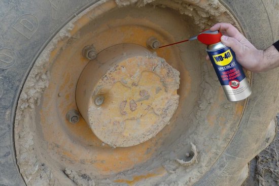 Man spuit WD-40 Specialist Super Kruipolie op de wielmoeren van een grote band.