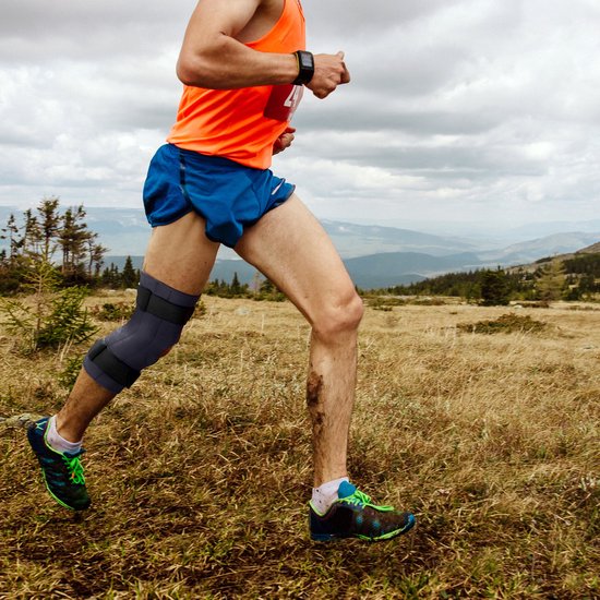 Man in oranje shirt en blauwe short met een Bracefox ErgoKnee 3 kniebrace tijdens het rennen buiten.