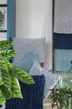 Een stapel gebreide kussens en plaids in blauw- en grijstinten. Een donkerblauw sierkussen ligt vooraan.