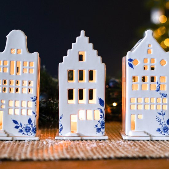 Close-up van drie witte keramische huisjes met blauwe bloemenprints, verlicht.