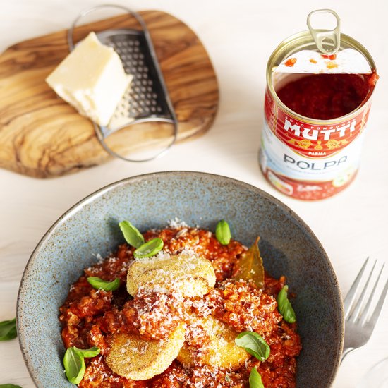 Blauwe schaal gevuld met rijst, tomatensaus, gehakt, geraspte kaas en basilicum. Naast een blik Mutti Polpa.