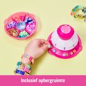 Een hand plaatst een kraal in de roze Pop Style Bracelet Maker, met kralenbakje ernaast.
